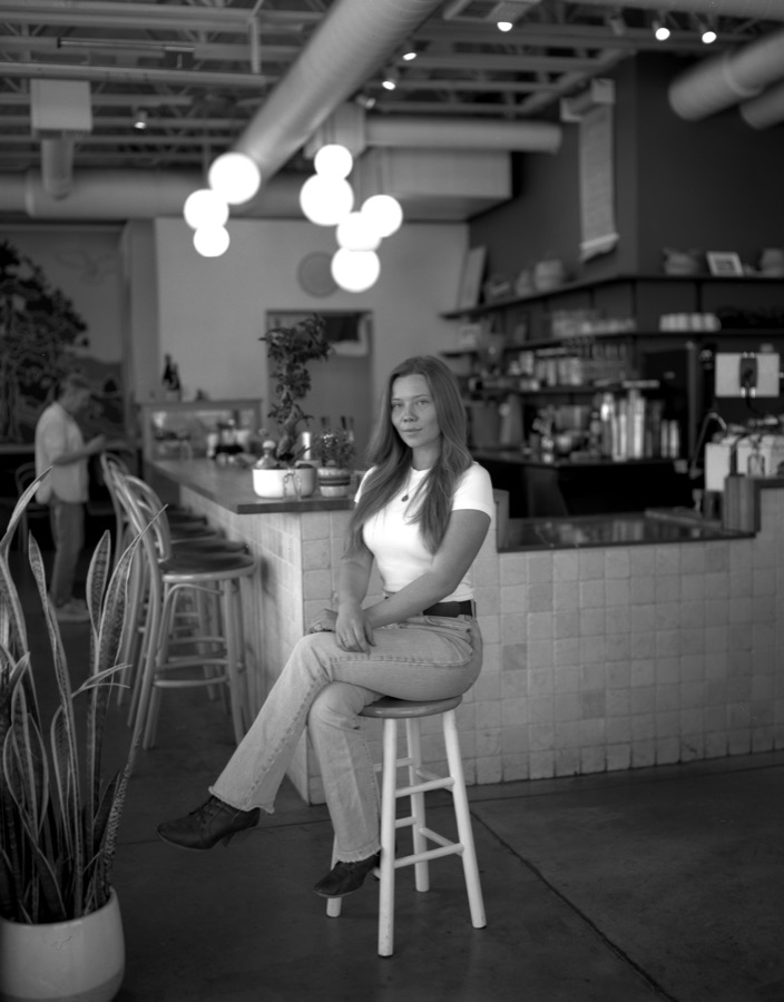 Aarica on a stool in a sunlit café, black and white