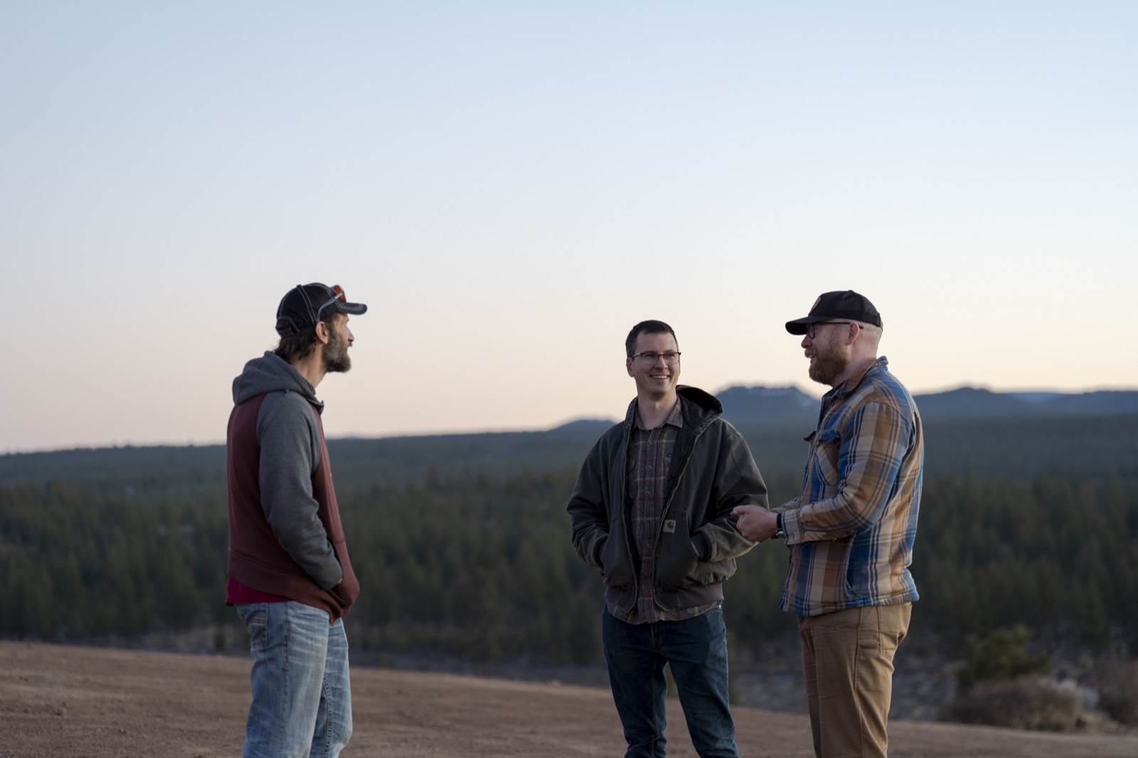 Three crew members talking on a ridge at dusk