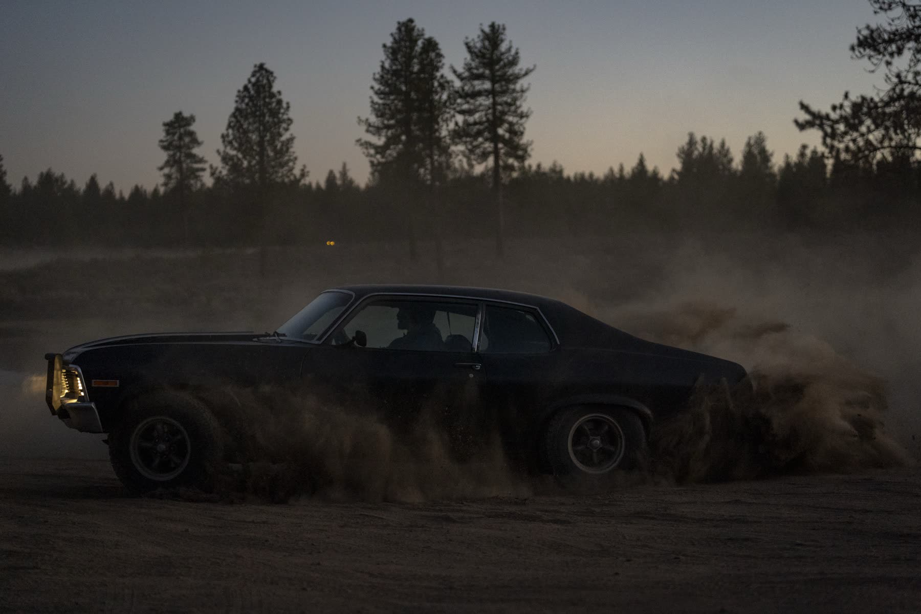 A classic muscle car sliding through dust at dusk