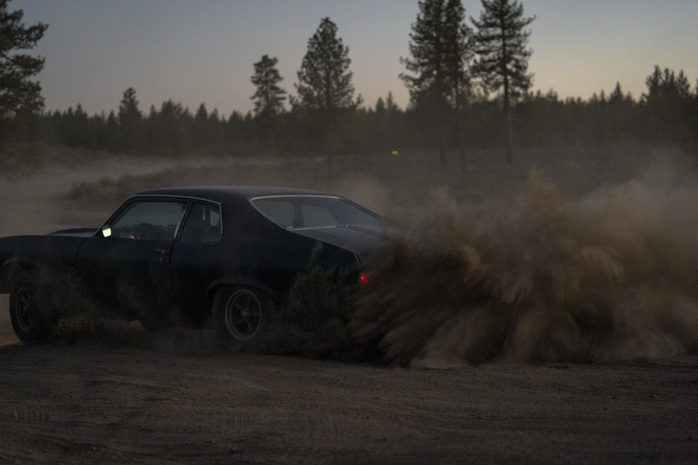 The muscle car kicking up a wall of dirt at dusk
