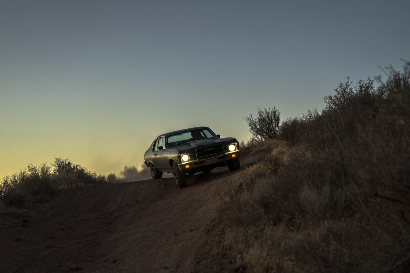 The car descending a tilted dirt road through sagebrush