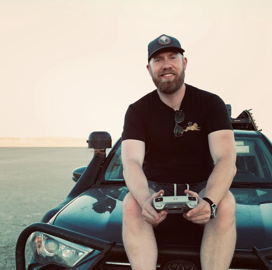 Robert seated on a truck hood holding a drone controller in the desert