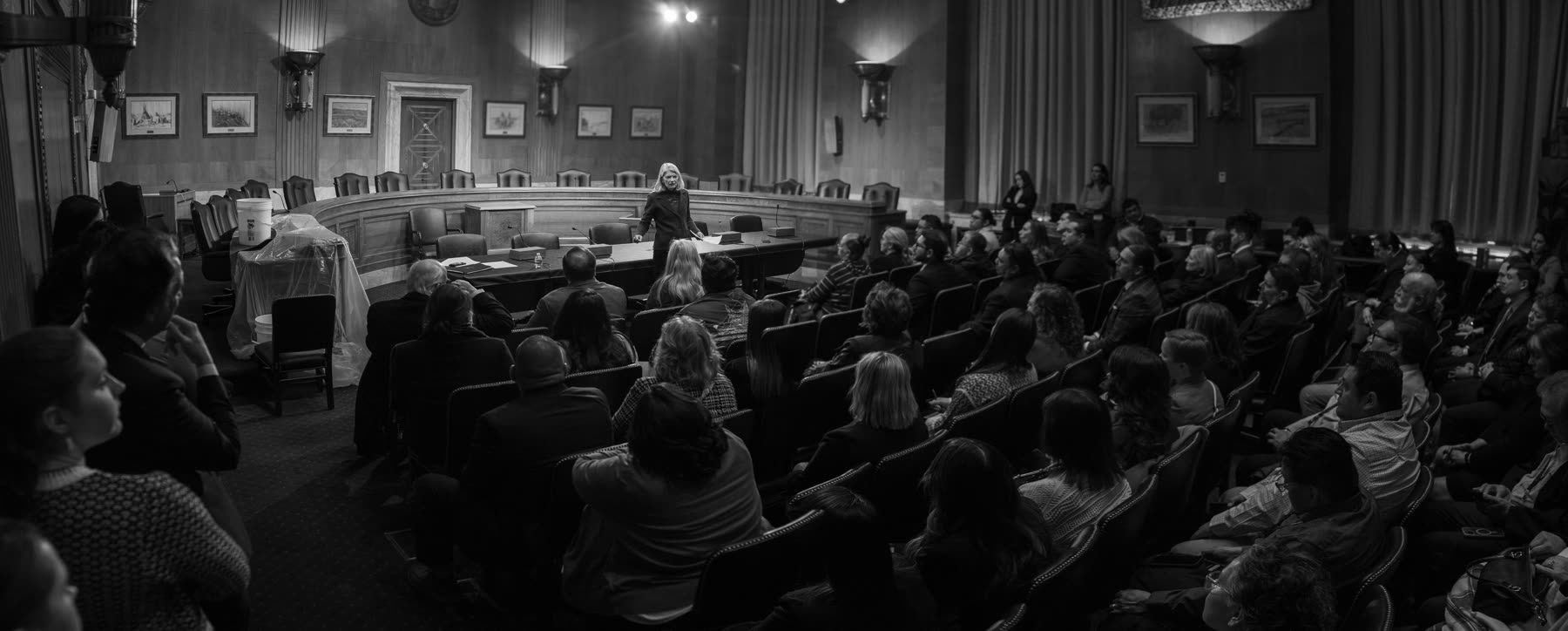 A senator addressing a full Senate hearing room, in black and white