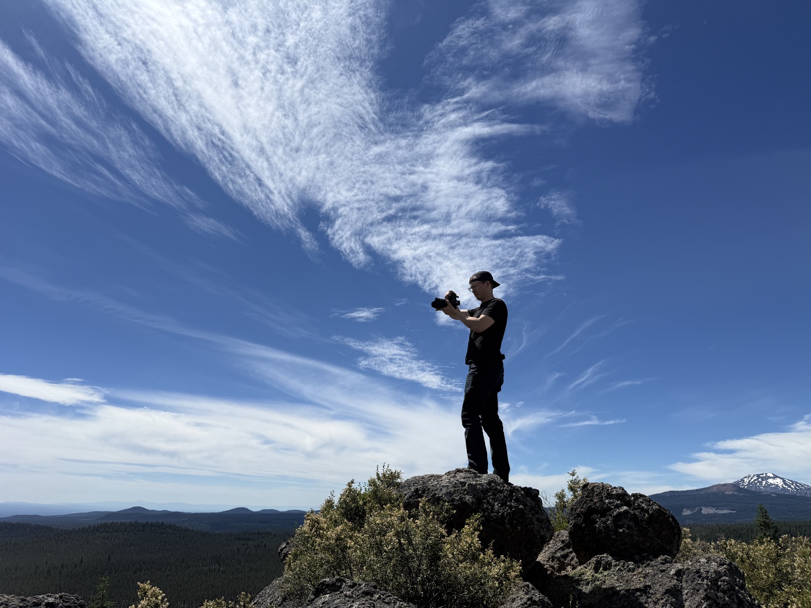 Tyler filming from a rocky summit under a big sky